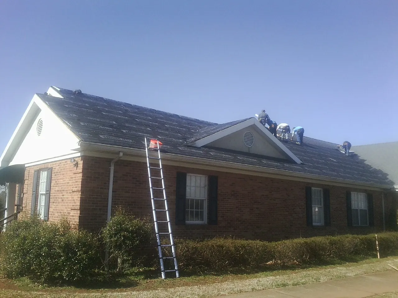 Crew tearing shingles off a brick ranch roof with a ladder set — Emergency Roof Repair work by our crew in Bartlett