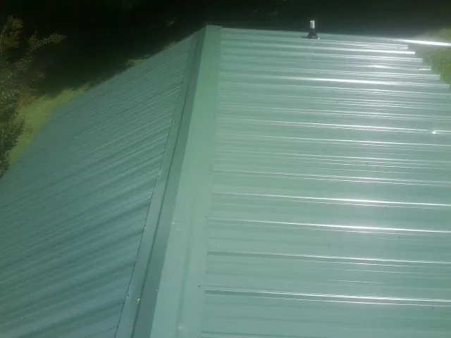 New green metal panels meeting at the ridge of a roof — Flat Roof Repair work by our crew in Bartlett