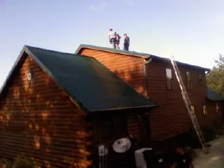 Crew on the ridge of a green metal roof on a two story log home in Bartlett